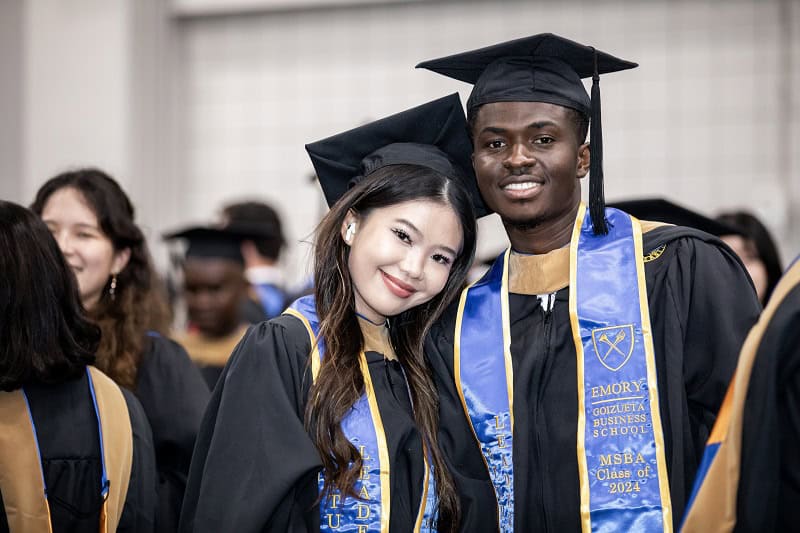 Two graduates in regalia pose together at Goizueta Commencement 2024