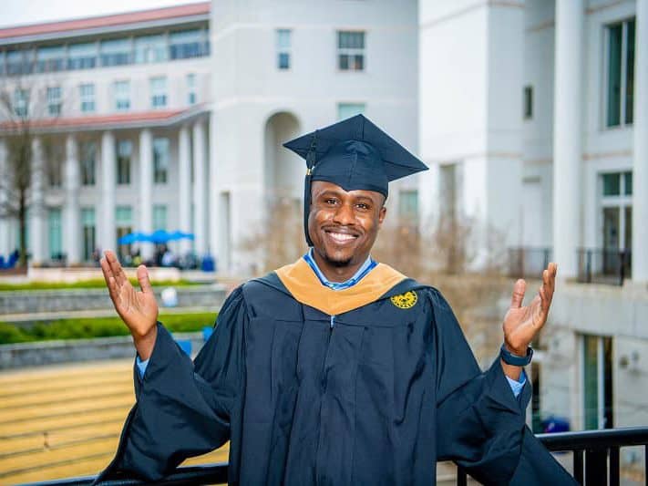 Goizueta's Henry Fumbah poses in front of the business school in commencement regalia